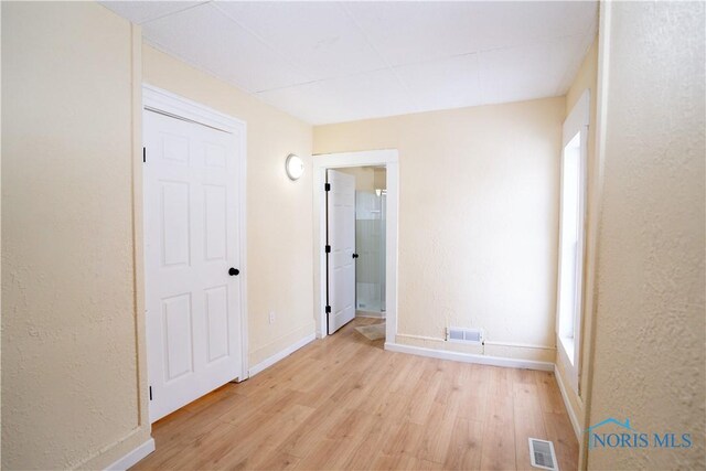 unfurnished bedroom with light wood finished floors, visible vents, a textured wall, connected bathroom, and baseboards