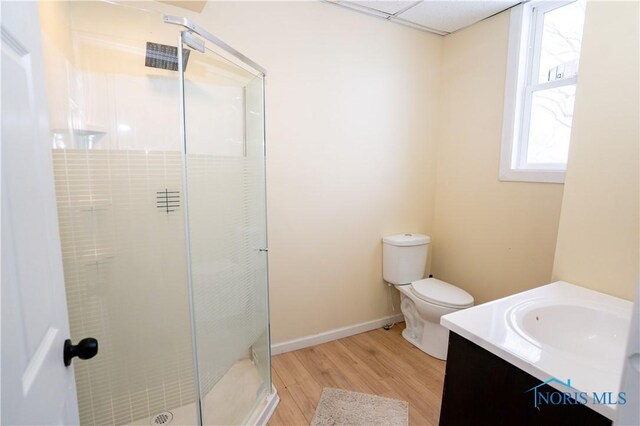 full bath featuring toilet, wood finished floors, vanity, baseboards, and a stall shower