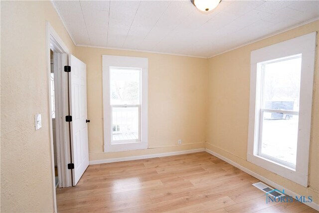 empty room featuring crown molding, baseboards, visible vents, and light wood-style floors