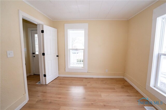 spare room with light wood finished floors, baseboards, visible vents, and ornamental molding