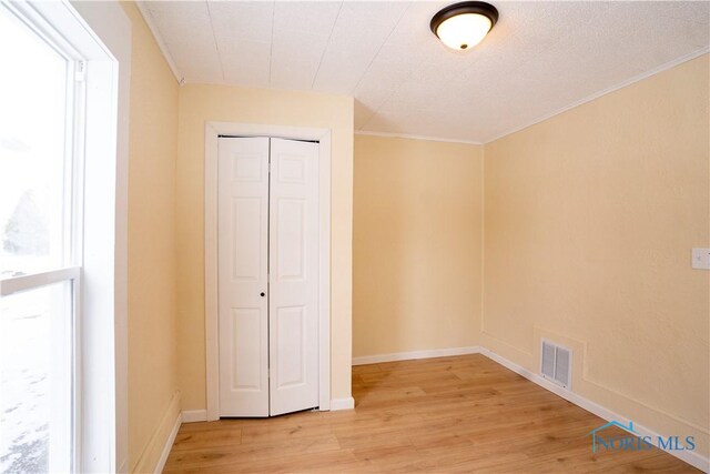 unfurnished bedroom with visible vents, baseboards, a closet, light wood-type flooring, and crown molding