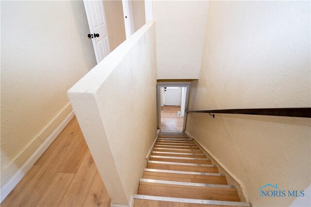 stairs with baseboards, wood finished floors, and a textured wall