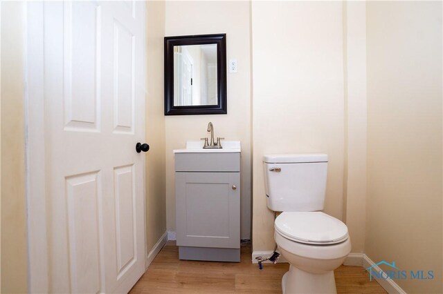 half bath featuring toilet, baseboards, wood finished floors, and vanity