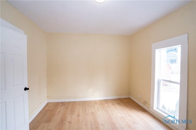 spare room with baseboards, a wealth of natural light, and light wood-style floors