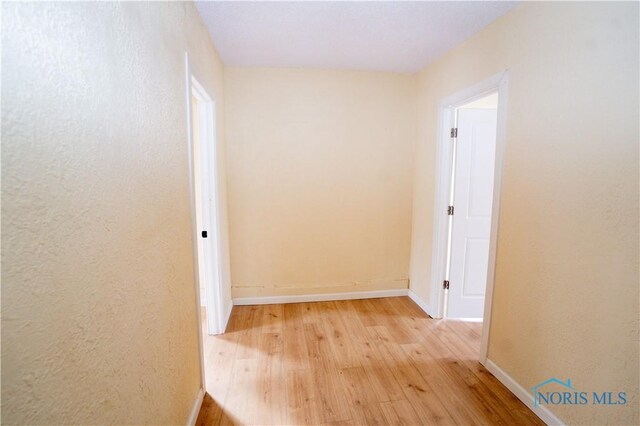 corridor with light wood-type flooring, baseboards, and a textured wall