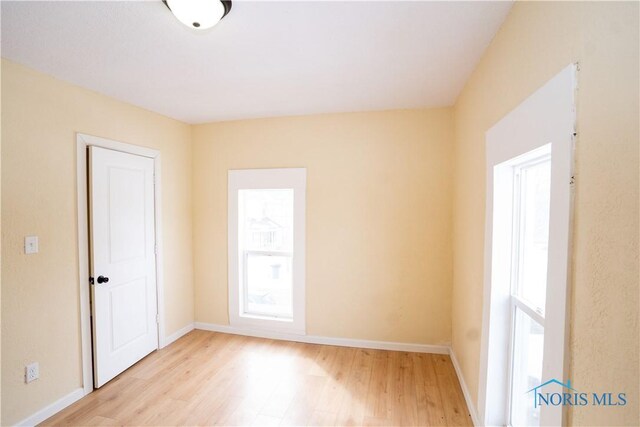 empty room with baseboards, light wood-type flooring, and a healthy amount of sunlight