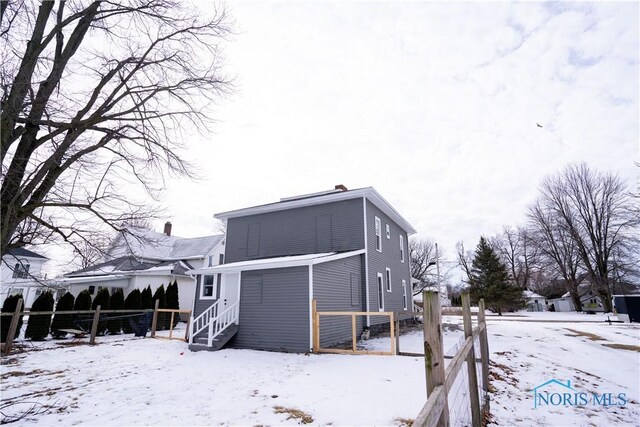 snow covered house featuring entry steps and fence