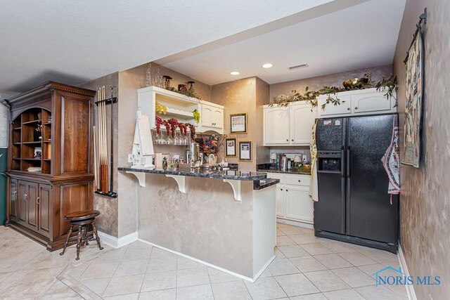 kitchen featuring kitchen peninsula, a kitchen breakfast bar, white cabinetry, dark stone counters, and black refrigerator with ice dispenser