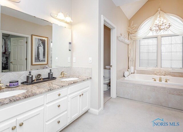 bathroom featuring tiled tub, vanity, an inviting chandelier, toilet, and vaulted ceiling