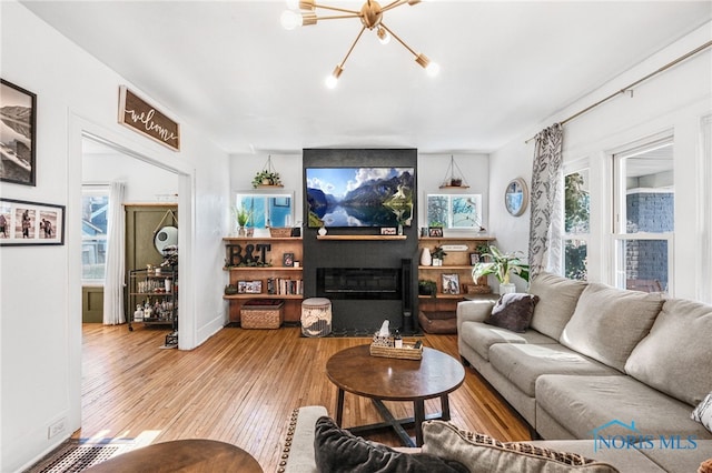 living room with baseboards, a chandelier, hardwood / wood-style floors, and a glass covered fireplace