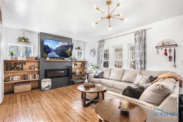 living room featuring hardwood / wood-style floors, a glass covered fireplace, and a notable chandelier