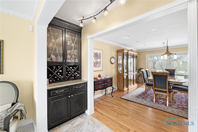 bar with a baseboard radiator, light hardwood / wood-style floors, hanging light fixtures, light stone counters, and crown molding