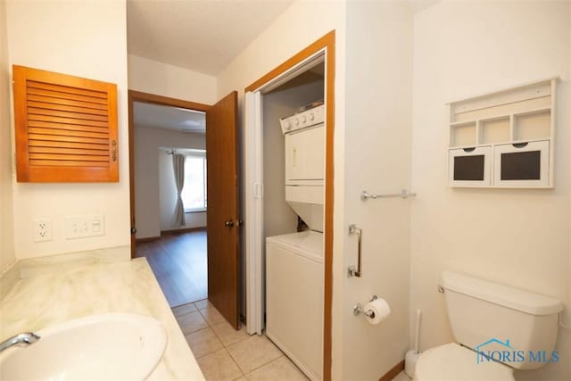 bathroom featuring tile patterned flooring, stacked washer and dryer, vanity, and toilet