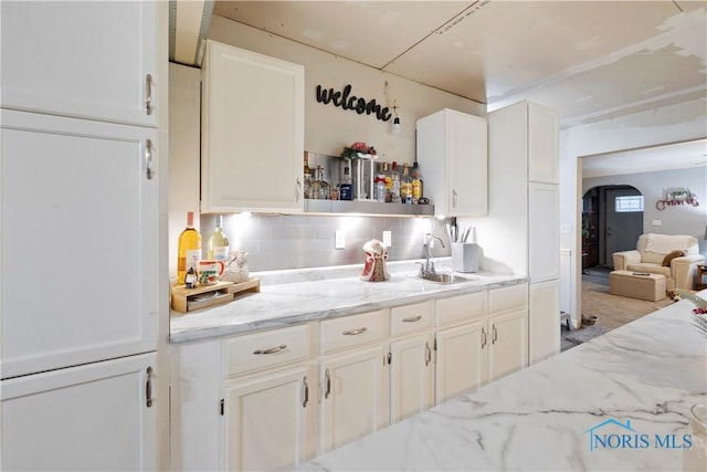 kitchen with white cabinets, backsplash, light stone countertops, and sink