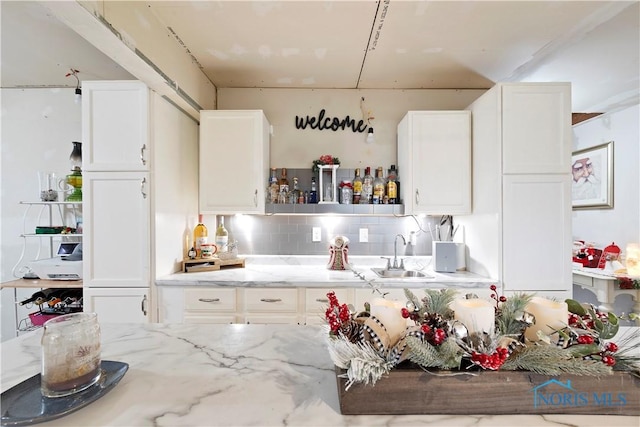 kitchen featuring light stone countertops, backsplash, white cabinets, and sink