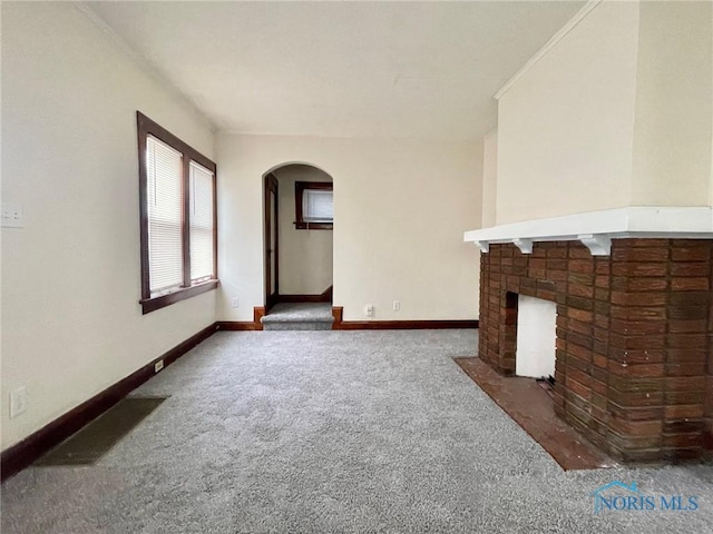 unfurnished living room with a brick fireplace and dark colored carpet