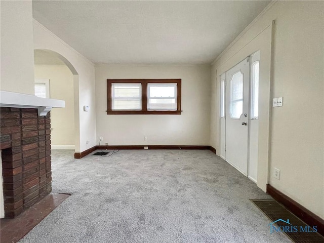 entryway with crown molding, light colored carpet, and a fireplace