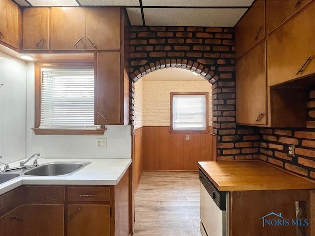 kitchen featuring dishwasher, brick wall, wooden walls, sink, and light hardwood / wood-style flooring