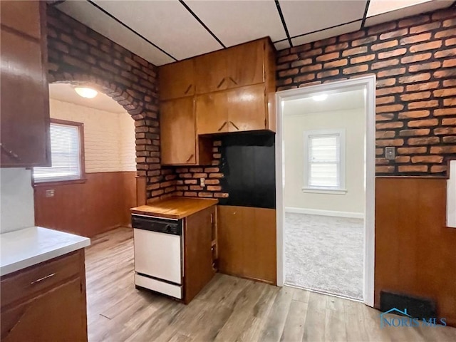 kitchen with white dishwasher, brick wall, wooden walls, and light wood-type flooring