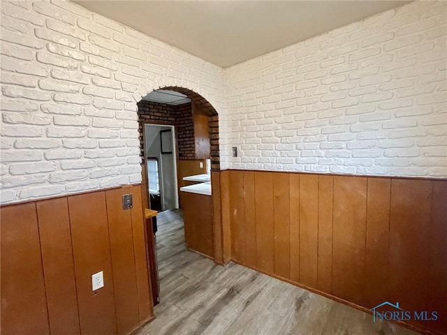 corridor with wooden walls, light hardwood / wood-style flooring, and brick wall