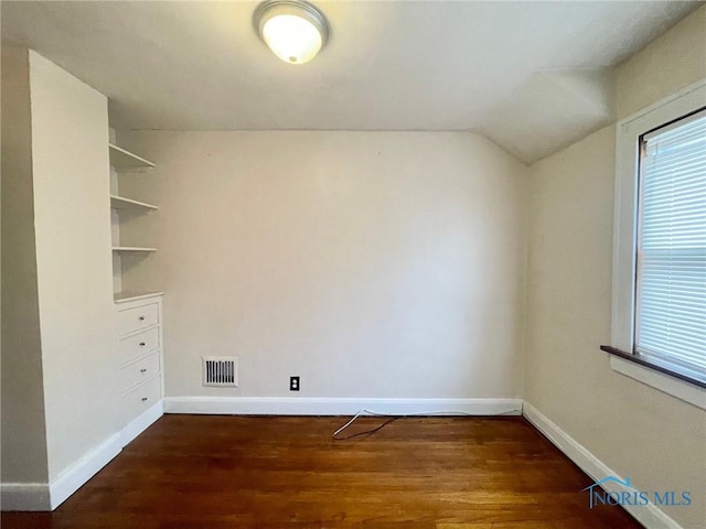 empty room featuring built in features, vaulted ceiling, and dark wood-type flooring