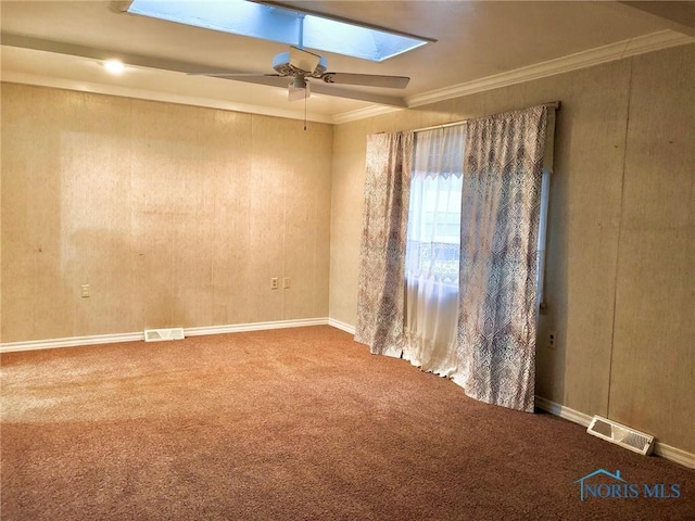 unfurnished room with a skylight, carpet, ceiling fan, and crown molding