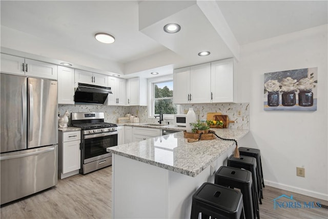 kitchen featuring light stone countertops, white cabinets, stainless steel appliances, kitchen peninsula, and light wood-type flooring