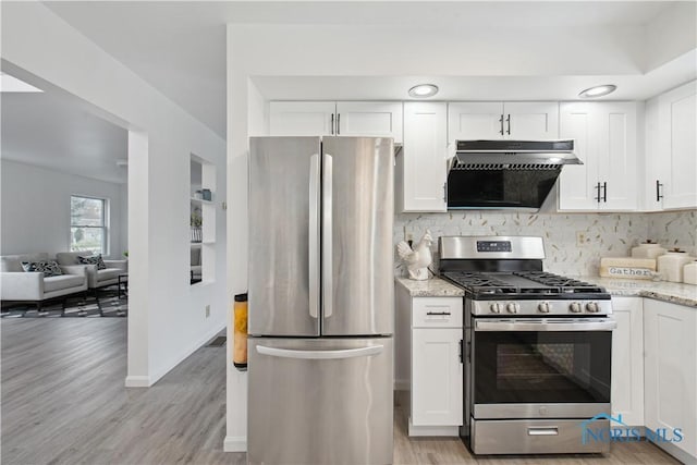 kitchen with light stone countertops, appliances with stainless steel finishes, white cabinetry, decorative backsplash, and light wood-type flooring