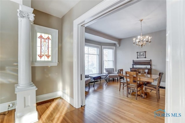 dining room with ornate columns, light hardwood / wood-style floors, and an inviting chandelier