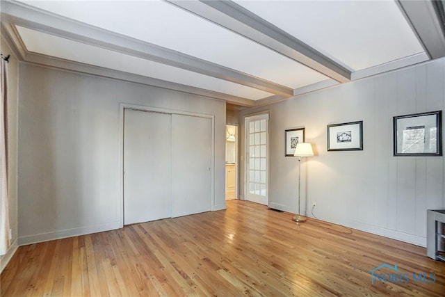 unfurnished bedroom featuring a closet, light wood-type flooring, and beam ceiling