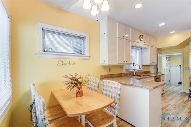 kitchen with kitchen peninsula, sink, white cabinetry, light stone counters, and light hardwood / wood-style floors