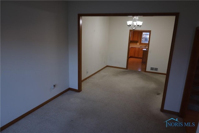 carpeted spare room featuring an inviting chandelier