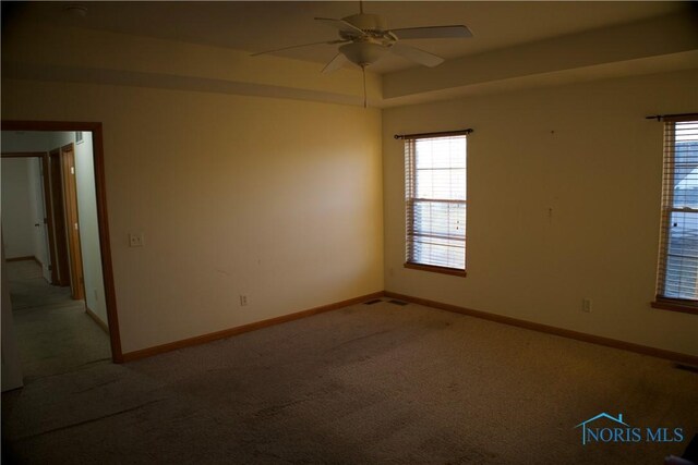 unfurnished room featuring a raised ceiling, ceiling fan, and carpet