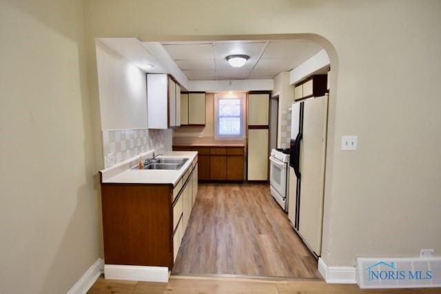 kitchen with white appliances, a paneled ceiling, tasteful backsplash, sink, and light hardwood / wood-style flooring