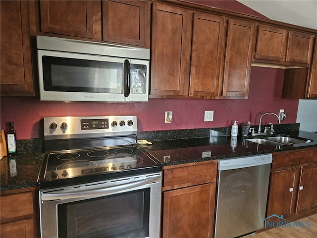 kitchen with stainless steel appliances, sink, light hardwood / wood-style flooring, and dark stone counters