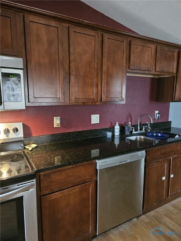 kitchen with light wood-type flooring, appliances with stainless steel finishes, sink, and dark stone countertops