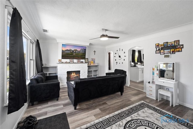 living room featuring crown molding, ceiling fan, hardwood / wood-style flooring, a fireplace, and a textured ceiling