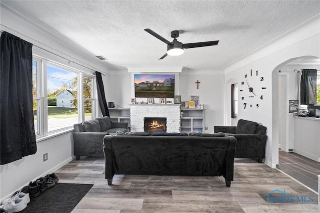 living room featuring crown molding, hardwood / wood-style flooring, a textured ceiling, and a stone fireplace