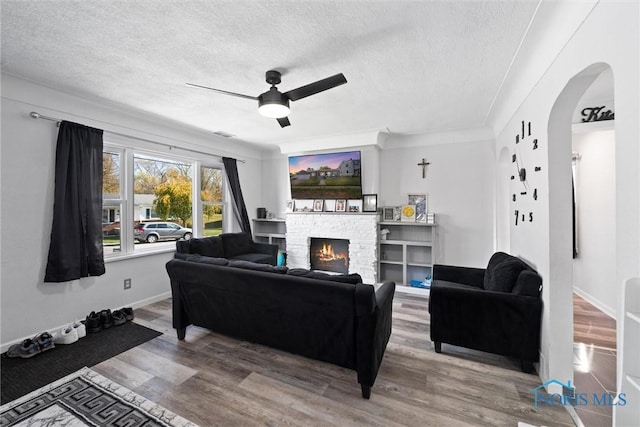 living room featuring ceiling fan, ornamental molding, a textured ceiling, and wood-type flooring