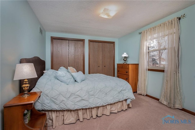 carpeted bedroom with two closets and a textured ceiling