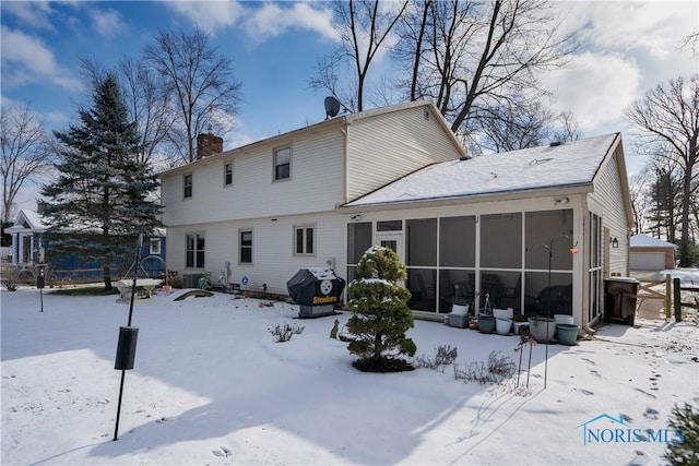 snow covered back of property featuring a sunroom