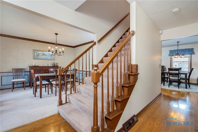 stairway featuring a notable chandelier, hardwood / wood-style floors, a textured ceiling, and crown molding