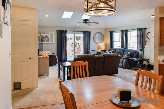 carpeted dining area featuring a textured ceiling, ceiling fan, and lofted ceiling with skylight