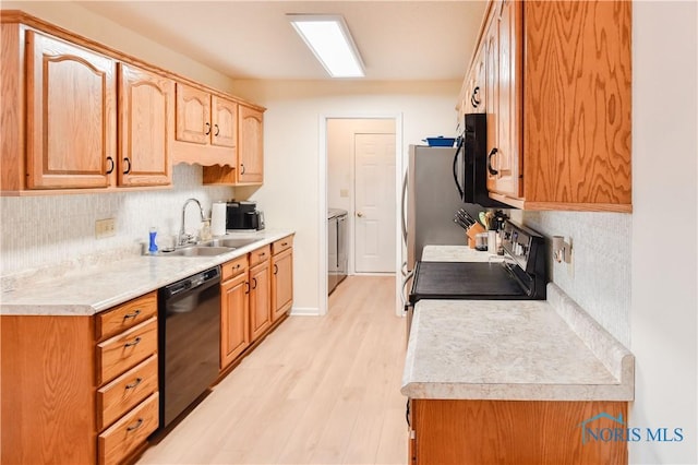 kitchen with black dishwasher, washing machine and clothes dryer, sink, light wood-type flooring, and electric range oven