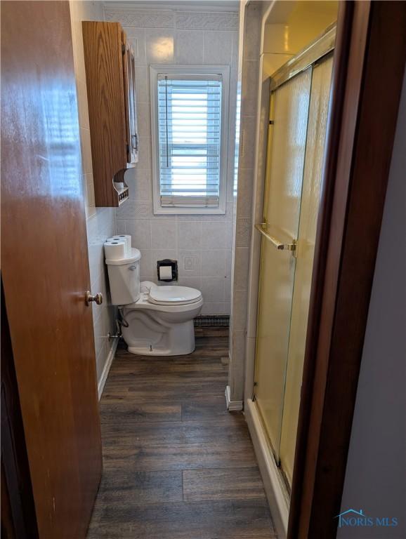 bathroom with wood-type flooring, toilet, tile walls, and a shower with shower door