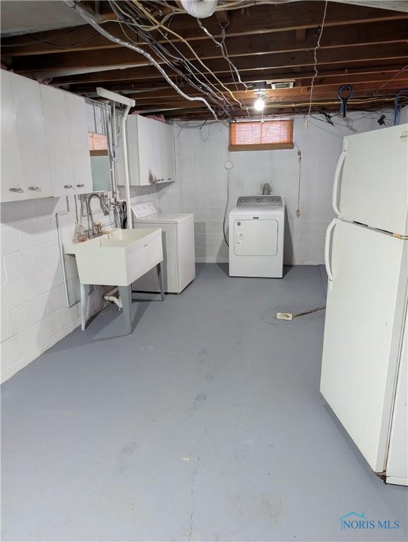 basement featuring sink, washing machine and clothes dryer, and white refrigerator