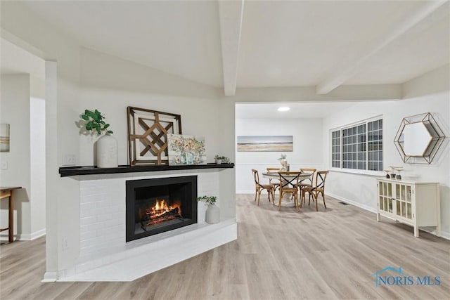 living room with a fireplace, beam ceiling, and light hardwood / wood-style floors