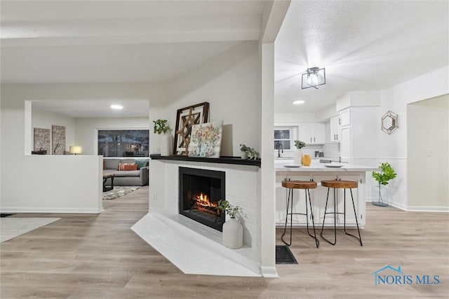 bar with tasteful backsplash, white cabinetry, a fireplace, and light wood-type flooring