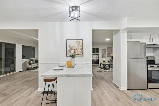 kitchen with a breakfast bar, tasteful backsplash, white cabinets, stainless steel appliances, and a textured ceiling