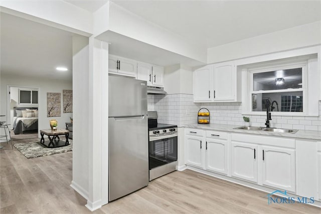 kitchen with sink, light wood-type flooring, appliances with stainless steel finishes, white cabinets, and backsplash